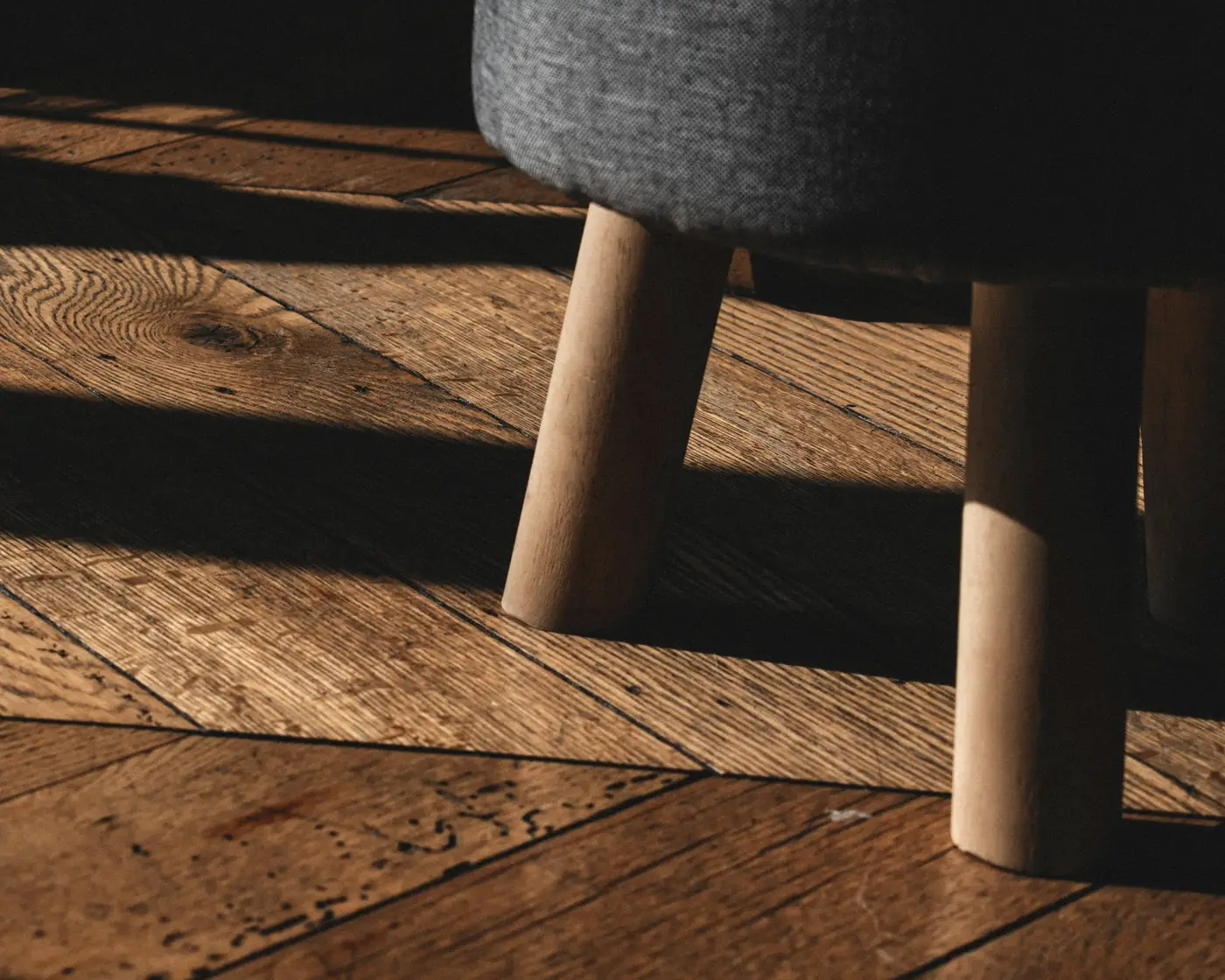 Lumière rasante sur un parquet en chêne, pieds d’un tabouret